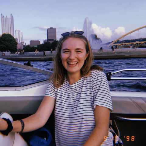 NHC PGH member Lexi smiling on a boat on a river with the Pittsburgh skyline in the background