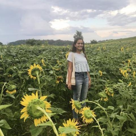 NHC PGH member Roosha smilling, standing in a sunflower field on an overcast day