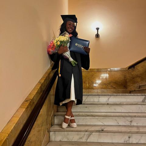 NHC member Chanita Russell wearing graduation attire while holding flowers, diploma, and smiling.