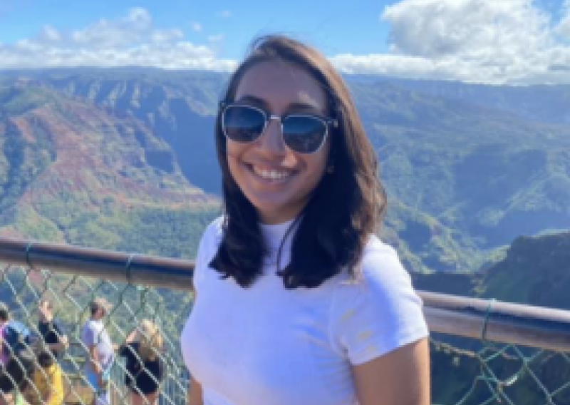NHC PGH member Chinmayi smiling on a sunny day with a scenic mountainous background wearing sunglasses