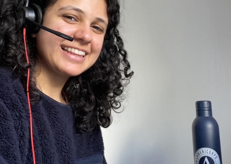 NHC SF member Saba Moussavian serving from home, wearing the audio headgear and microphone. An AmeriCorps water bottle is seen in the background against a white background.
