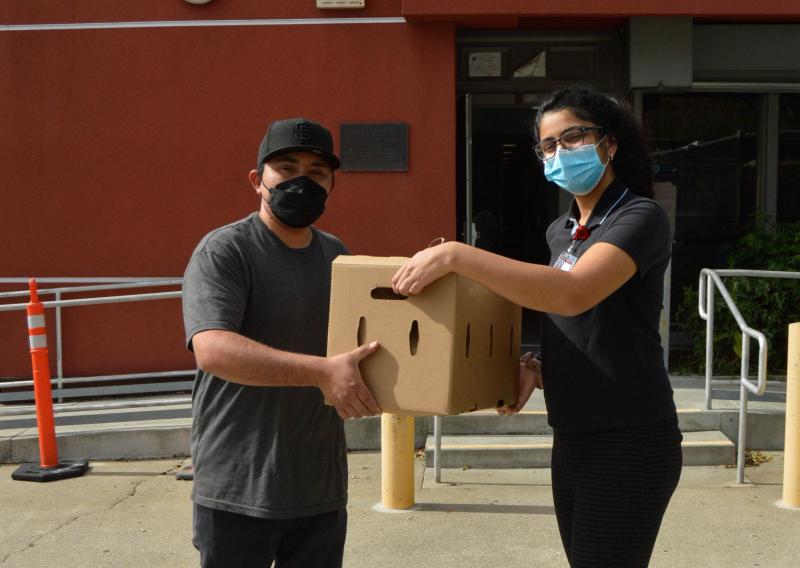 Saadhana Deshpande (right) holding a box of produce together with M. O. (left), one of the drivers for one of the produce delivery companies that aids the FAMC.