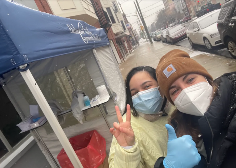 two people with masks on in front of a covid testing tent on a snowy day