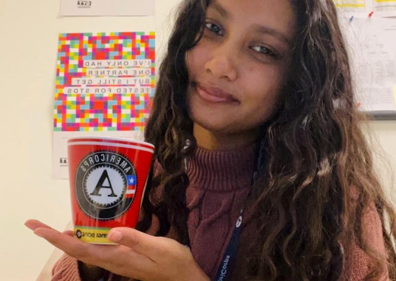 Aneesha holding a mug with the AmeriCorps logo on it