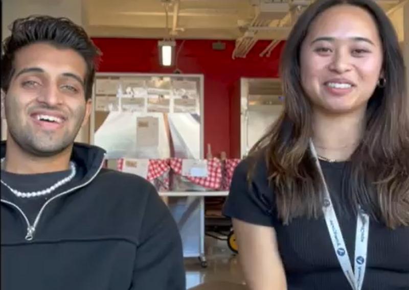 Abhi (left) and Laurel (right) sit in front of the camera, facing the camera and smiling. 