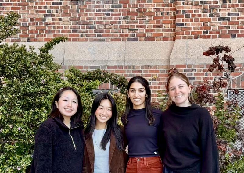 Lilian, Sam, Anisha, and Morgan are seen standing in the middle of the frame, facing the camera and smiling. 