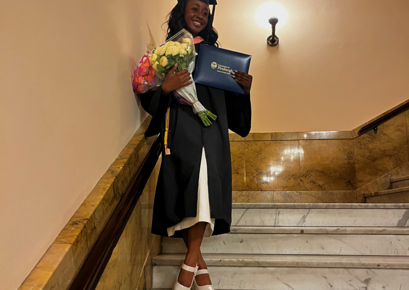 NHC member Chanita Russell wearing graduation attire while holding flowers, diploma, and smiling.