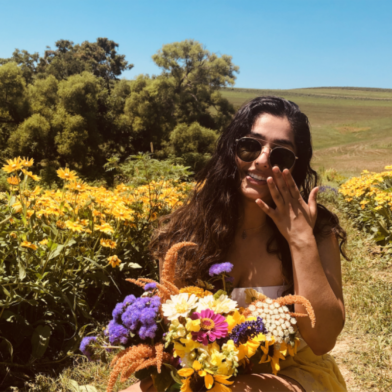 NHC PGH member Medha smiling in a field of flowers with sunglasses on and holding flowers