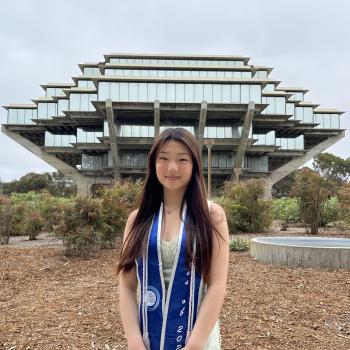 Sian Hong is standing in the middle frame, her arms crossed in front of her. She is wearing a graduation stole. Behind her is a beautiful ornate building in the background.