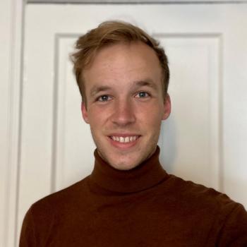 John Hansen is facing the camera and smiling. He is wearing a burgundy turtle neck.