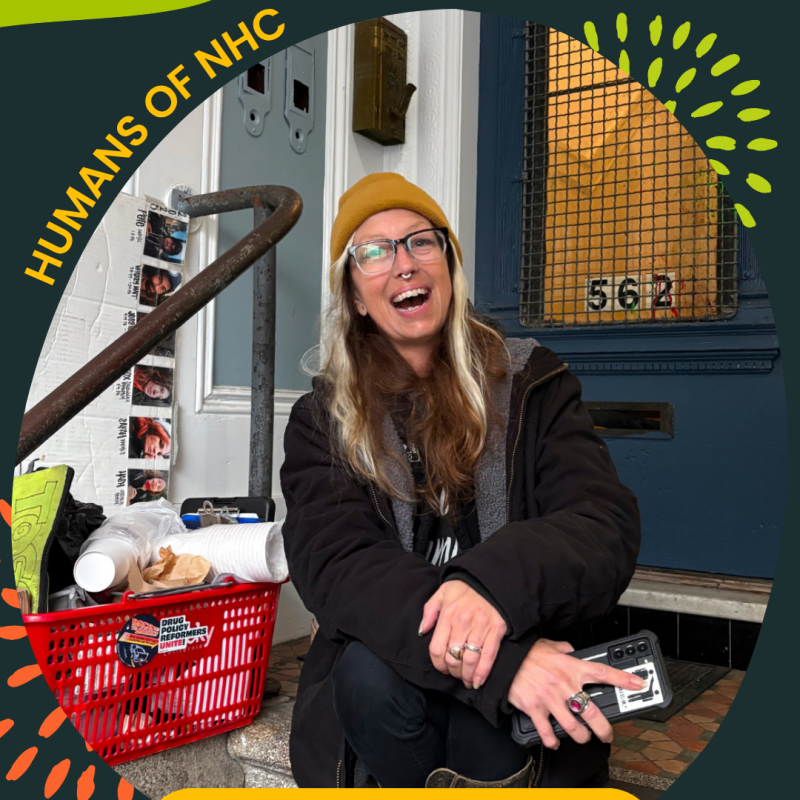 A frame with the text "Humans of NHC" and "Mary, Program Director, Homeless Youth Alliance" circles the photo of a woman sitting on the top of a staircase leading to a front door. She is facing the camera and smiling. Next to her right arm is a grocery basket filled with materials, including compostable cups and tote bags, among other resources.