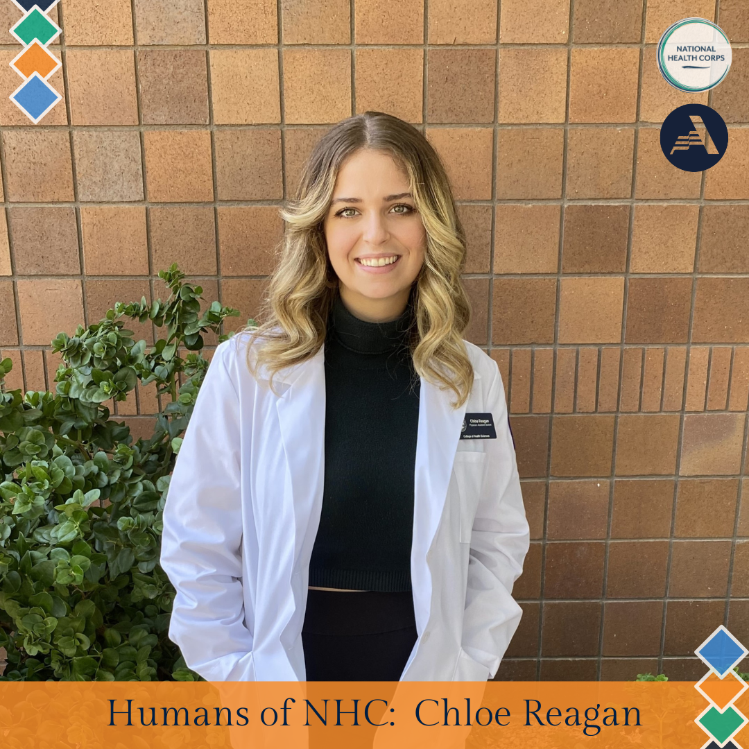 Chloe Reagan stands in the middle of the frame, facing the camera and smiling. Chloe is wearing a white coat over a black turtleneck. 