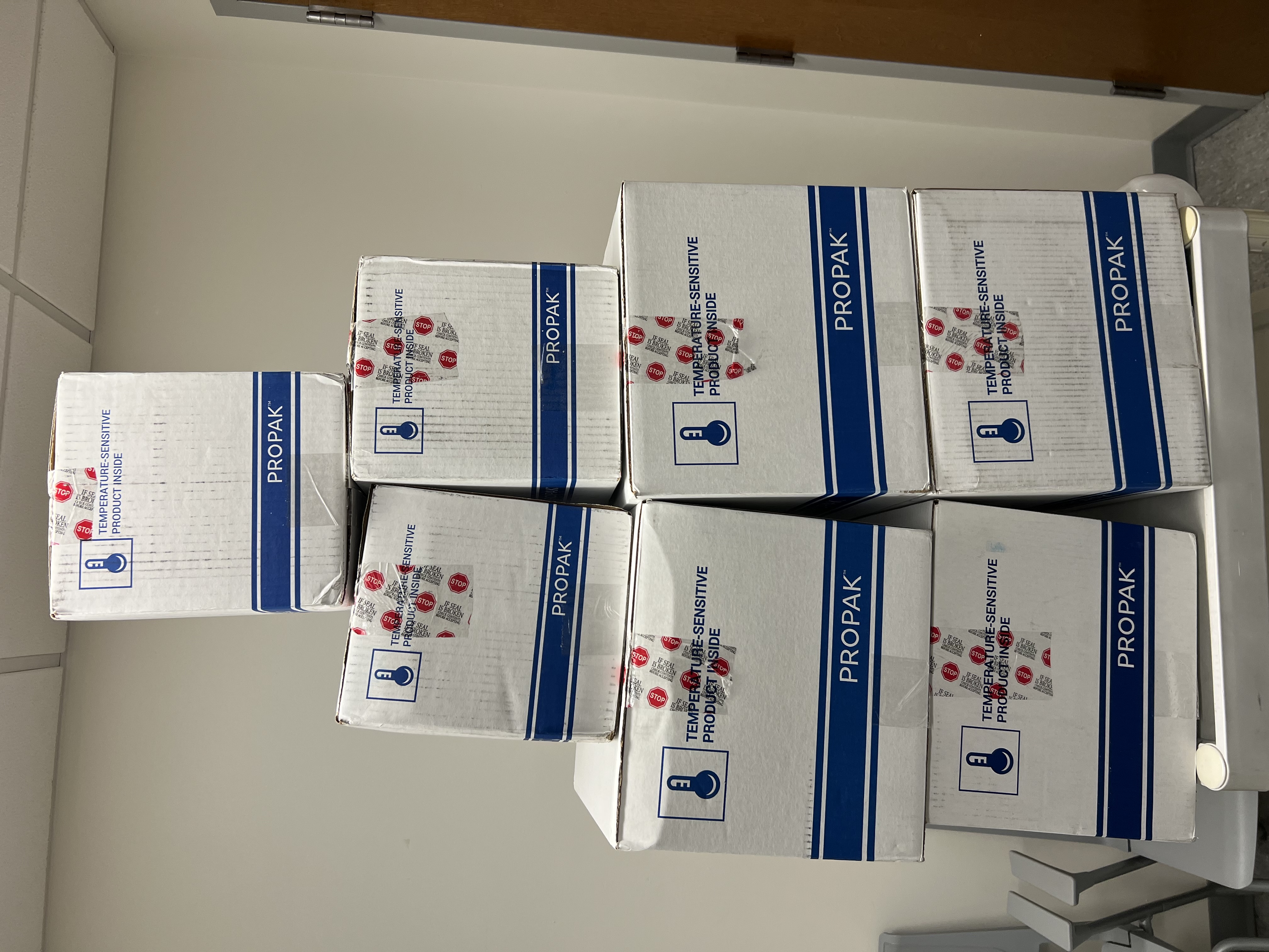 A stack of 7 white and blue boxes that are temperature sensitive