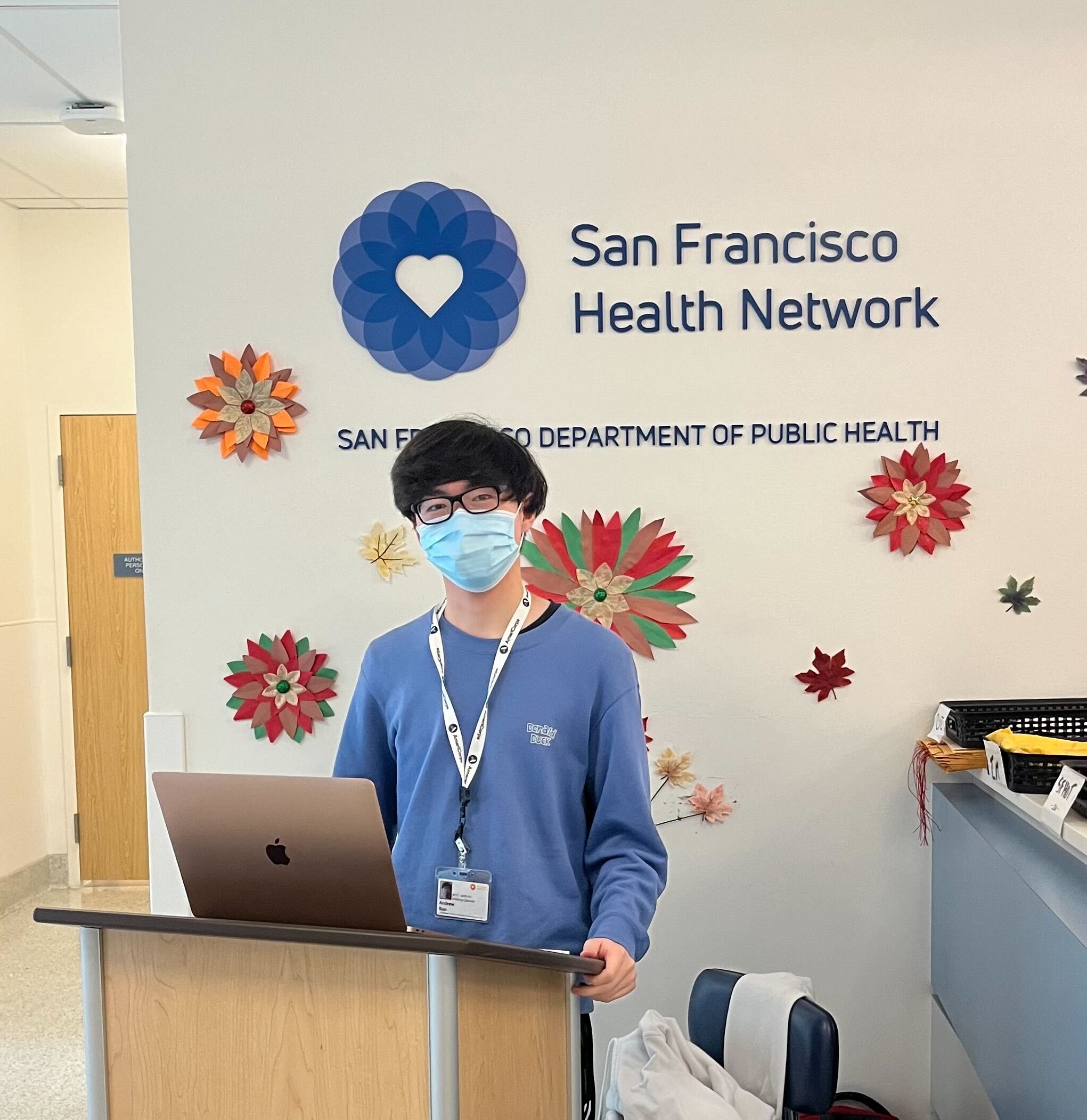 A person stands behind the podium facing the camera. Behind the person is a wall with the San Francisco Health Network logo.