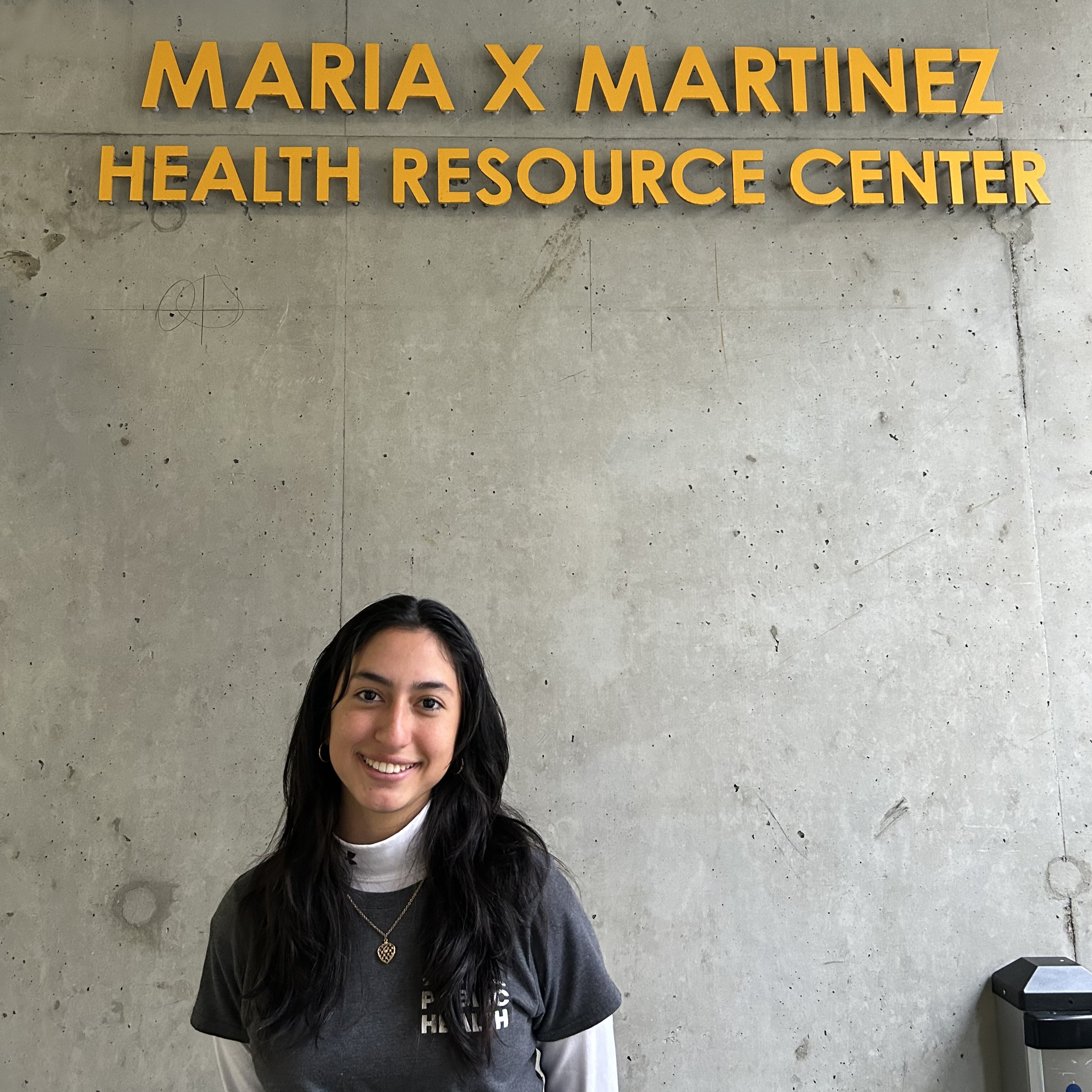 Laura is standing off center frame below a sign reading Maria X Martinez Health Resource Center.