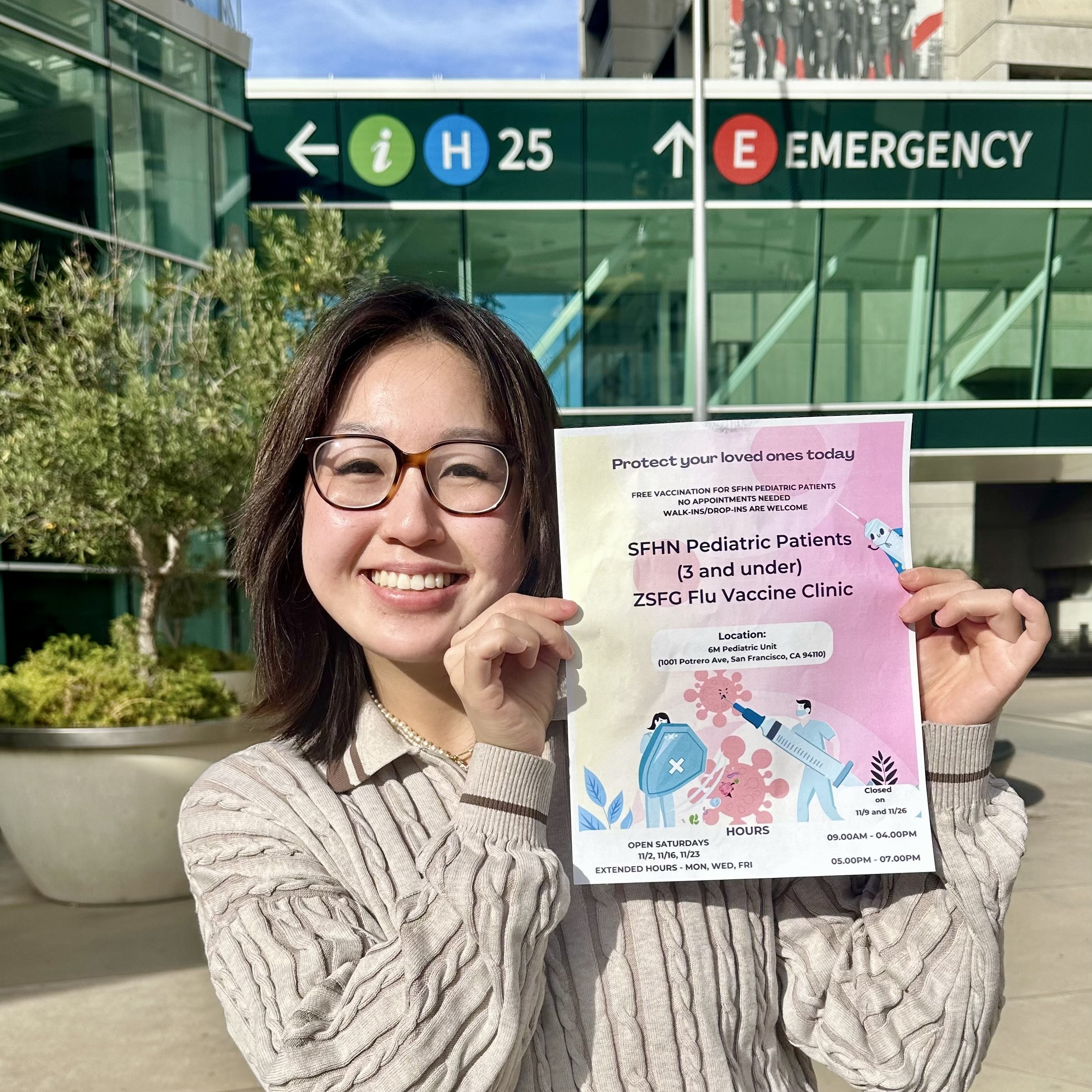 Lilian poses with a flyer announcing a Pediatric Patients Flu Vaccine Clinic at Zuckerberg San Francisco General. 