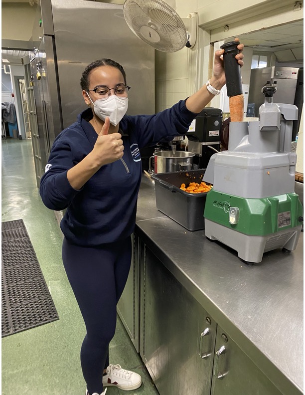 Juliet wearing a mask in a kitchen while preparing food at a local organization