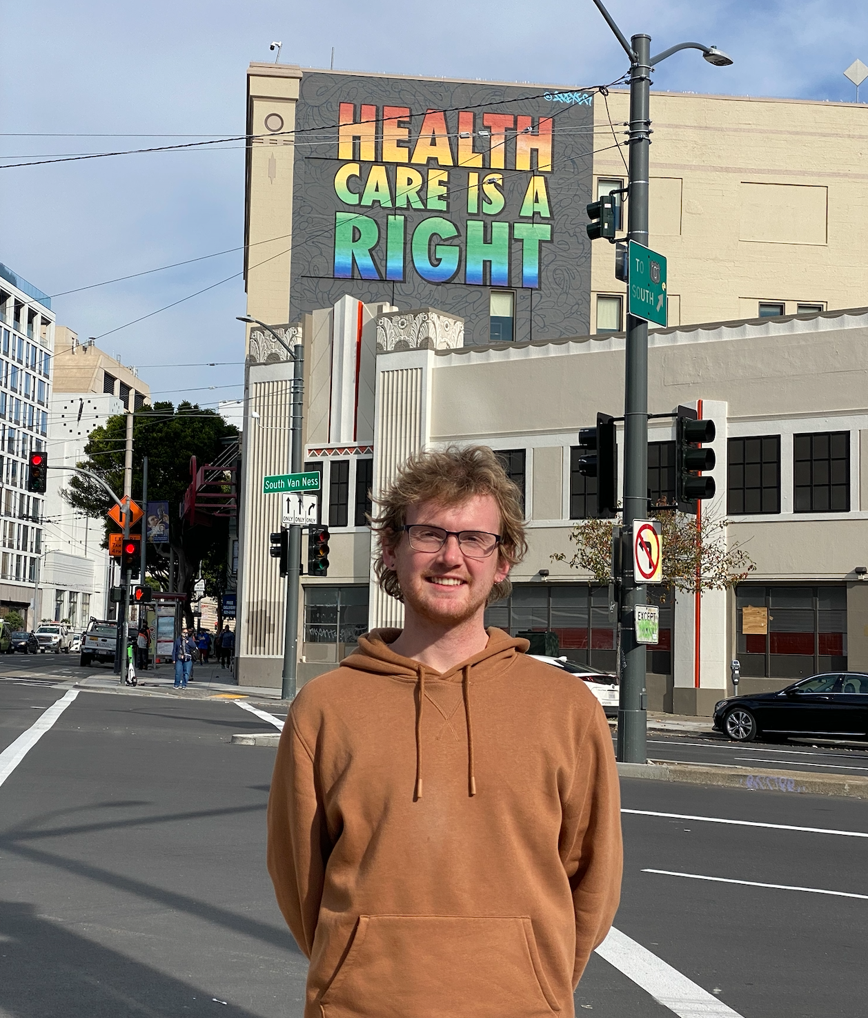 Will stands in front of the Health Care is a Right mural near HealthRIGHT 360.