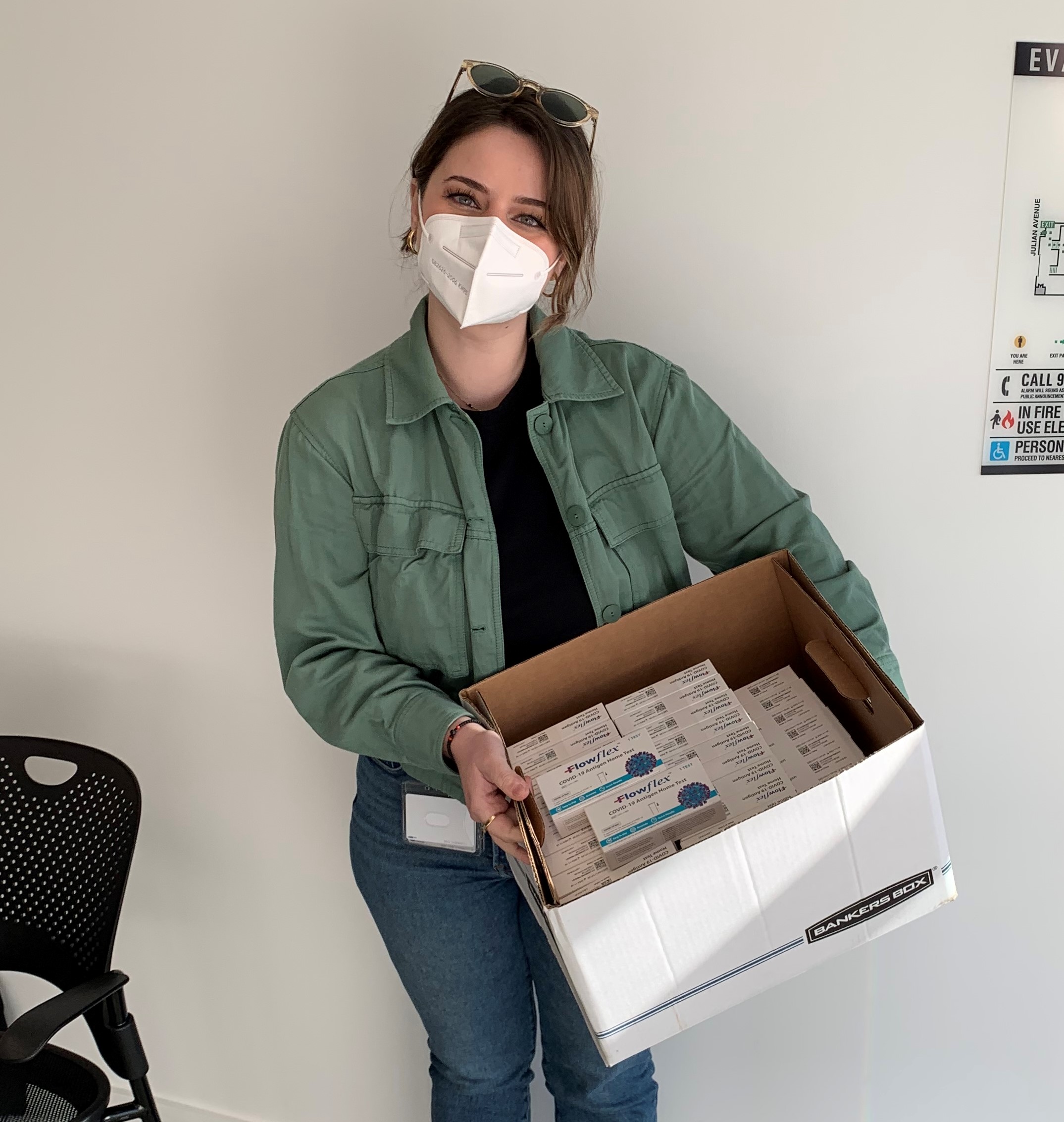 Vjola Jorgji is facing the camera directly. She is wearing a facmask. She is holding a box with Rapid COVID-19 tests to be distributed to patients.