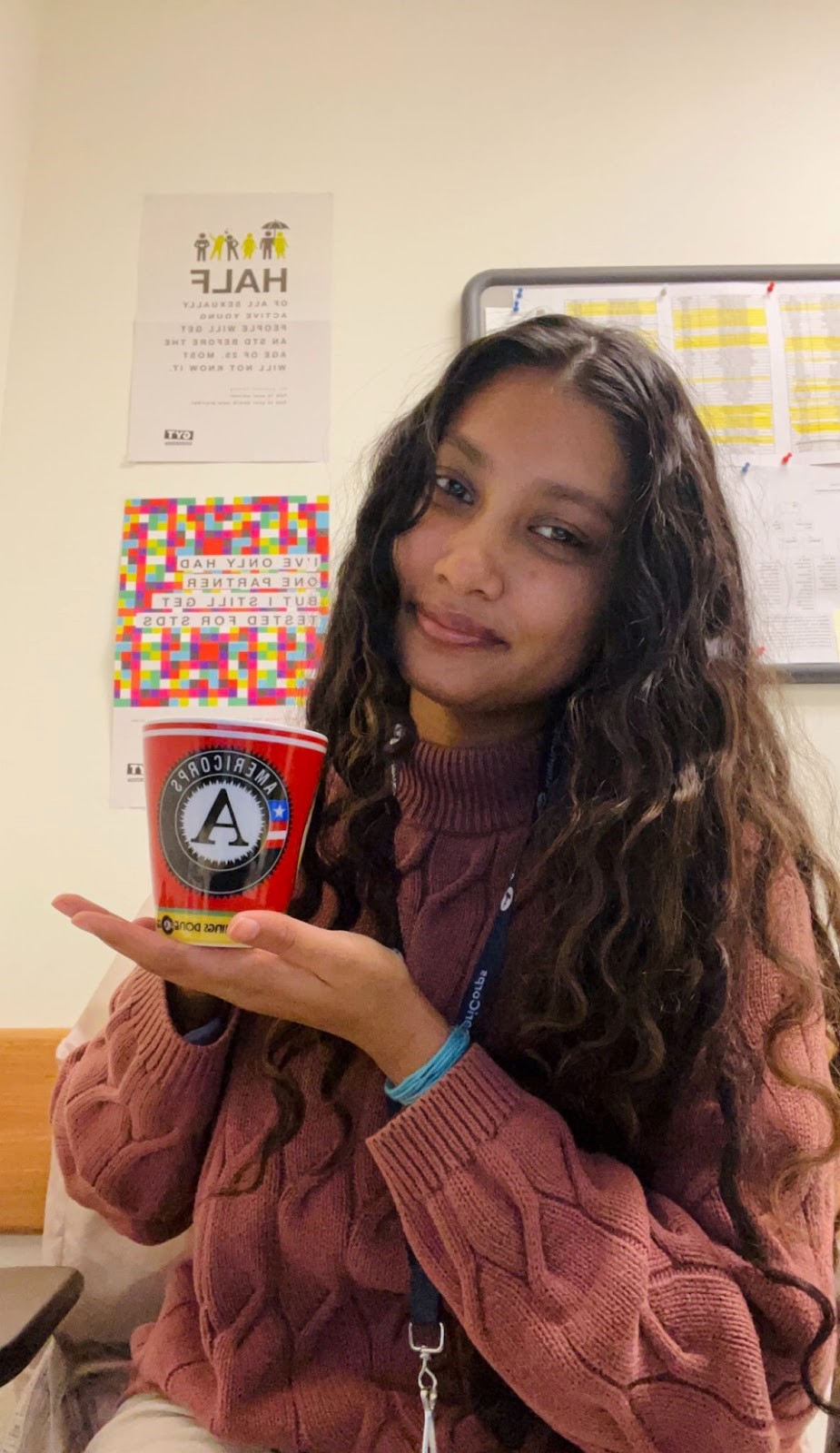 A photo of Aneesha holding a mug with the AmeriCorps logo on it